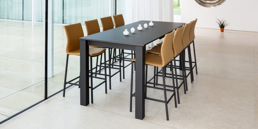 Moderne hoge eettafel met zwarte bovenkant en acht leren barstoelen in mosterdkleur, verkrijgbaar bij Belga Meubel Brugge